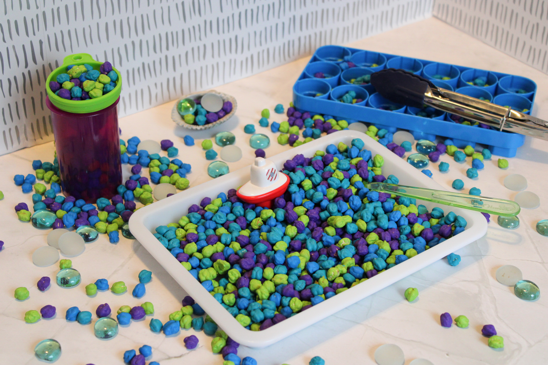 chickpea sensory bin with aqua colored chickpeas and under the sea toys on a counter