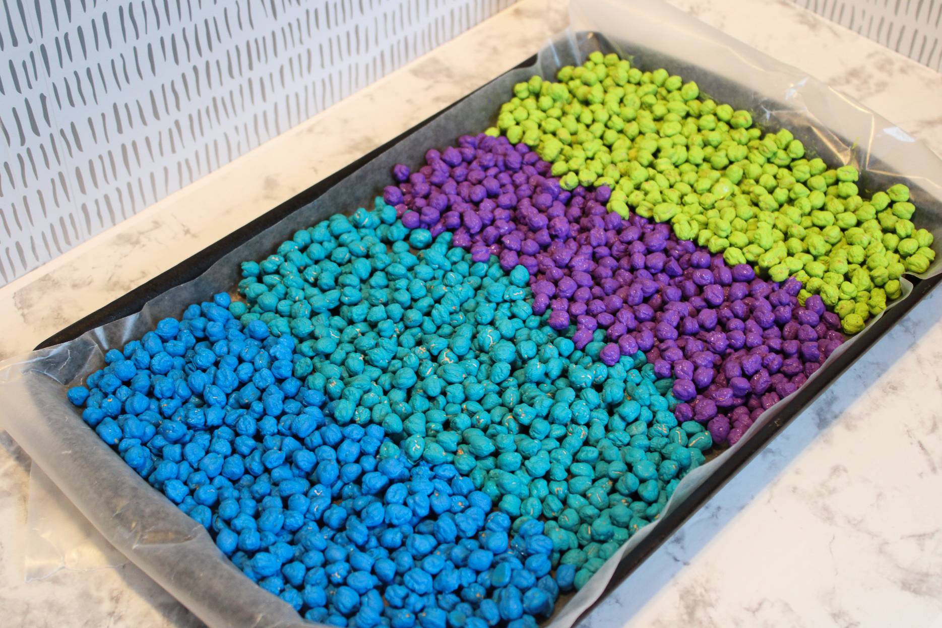 cookie sheet on a counter lined with wax paper with painted chickpeas layered on top